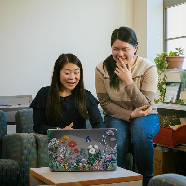 两个学生看着一个贴着花的笔记本电脑，对他们看到的东西笑了.